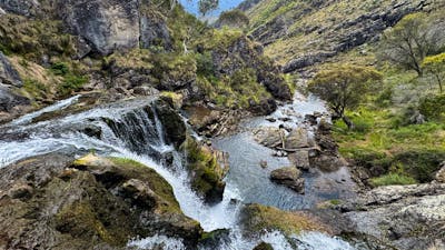 The top of a waterfall with some rocks and a pool of water at the bottom.