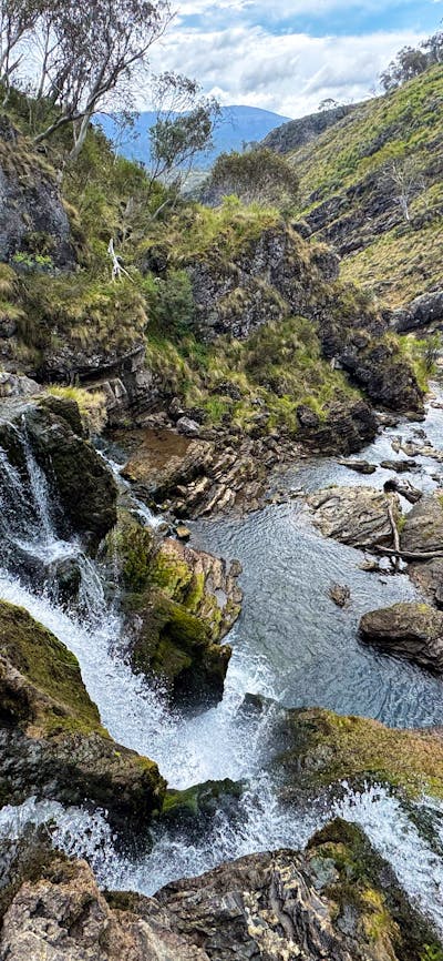 The top of a waterfall with some rocks and a pool of water at the bottom.