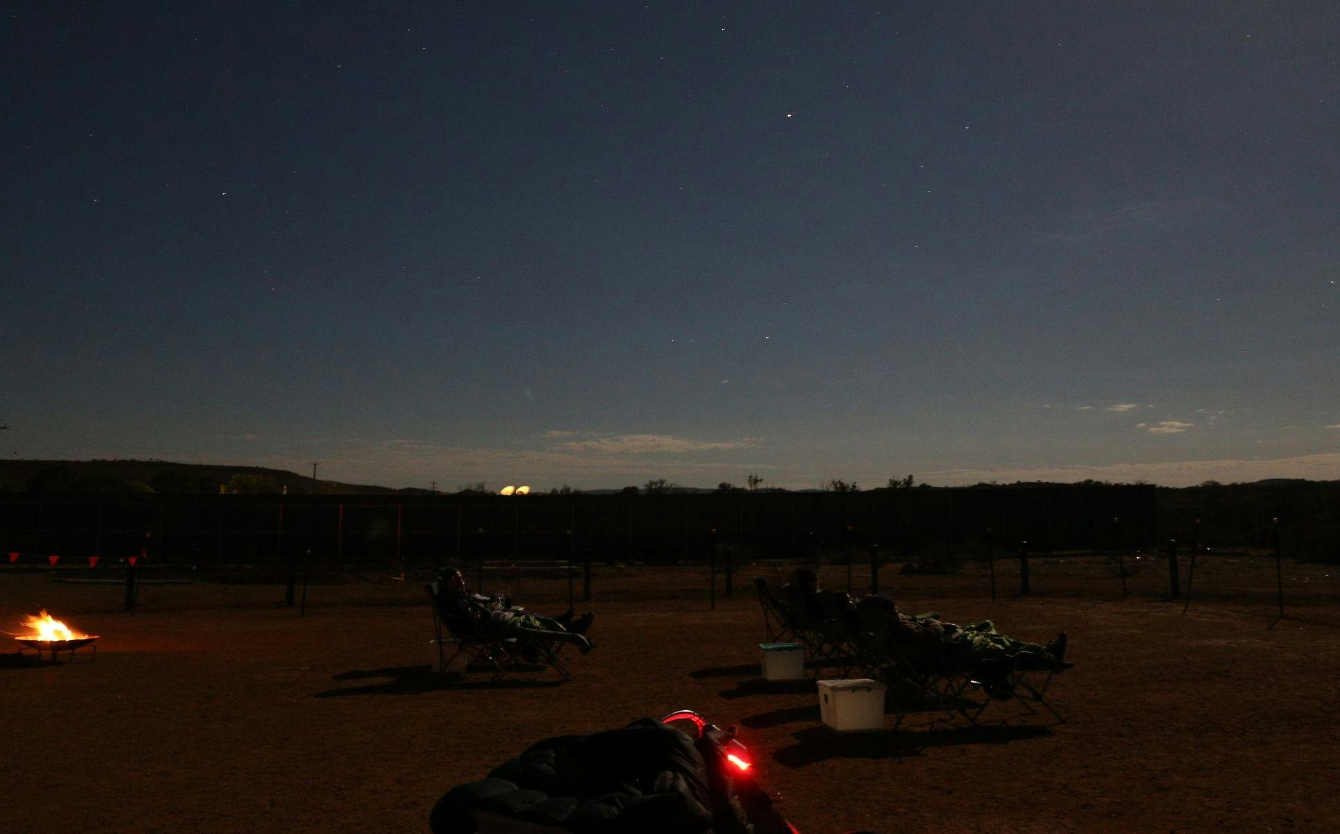 People in reclined chairs gazing at moonlit sky