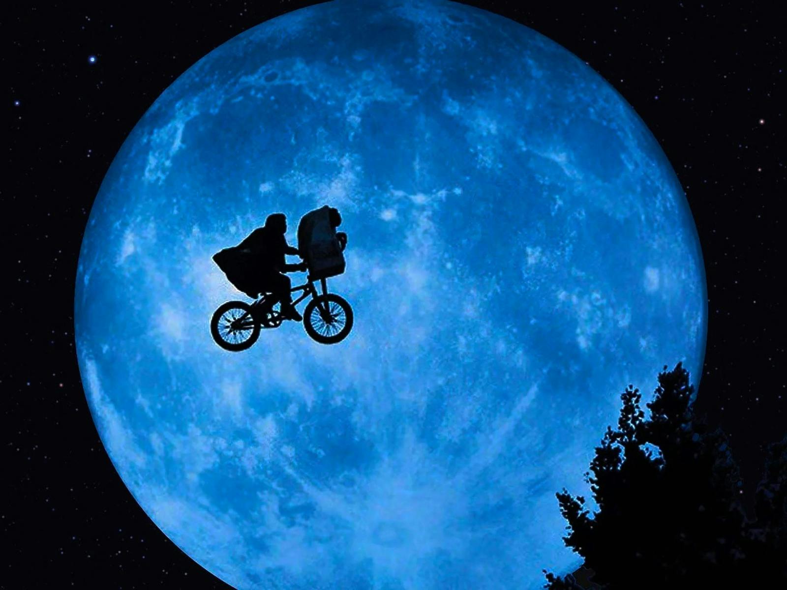 A shadow image of a person in a cape on a bike cycling across the sky in front of a large planet