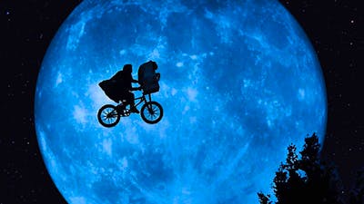 A shadow image of a person in a cape on a bike cycling across the sky in front of a large planet
