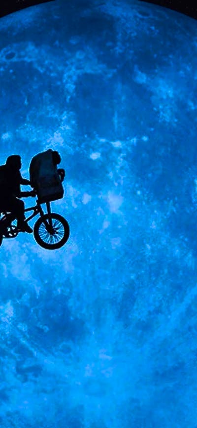 A shadow image of a person in a cape on a bike cycling across the sky in front of a large planet