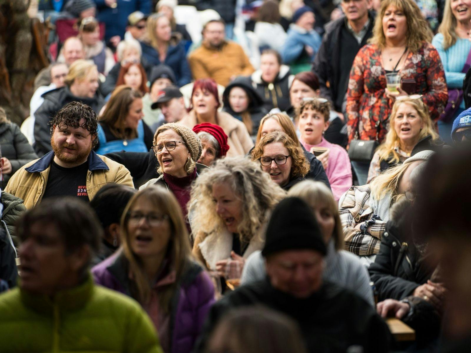 Close-up of an outdoor crowd with many people singing or cheering with open mouths