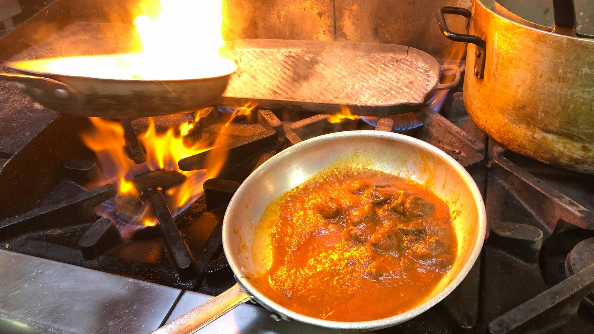 Shot of meals being cooked  over stove top with flames and pans.