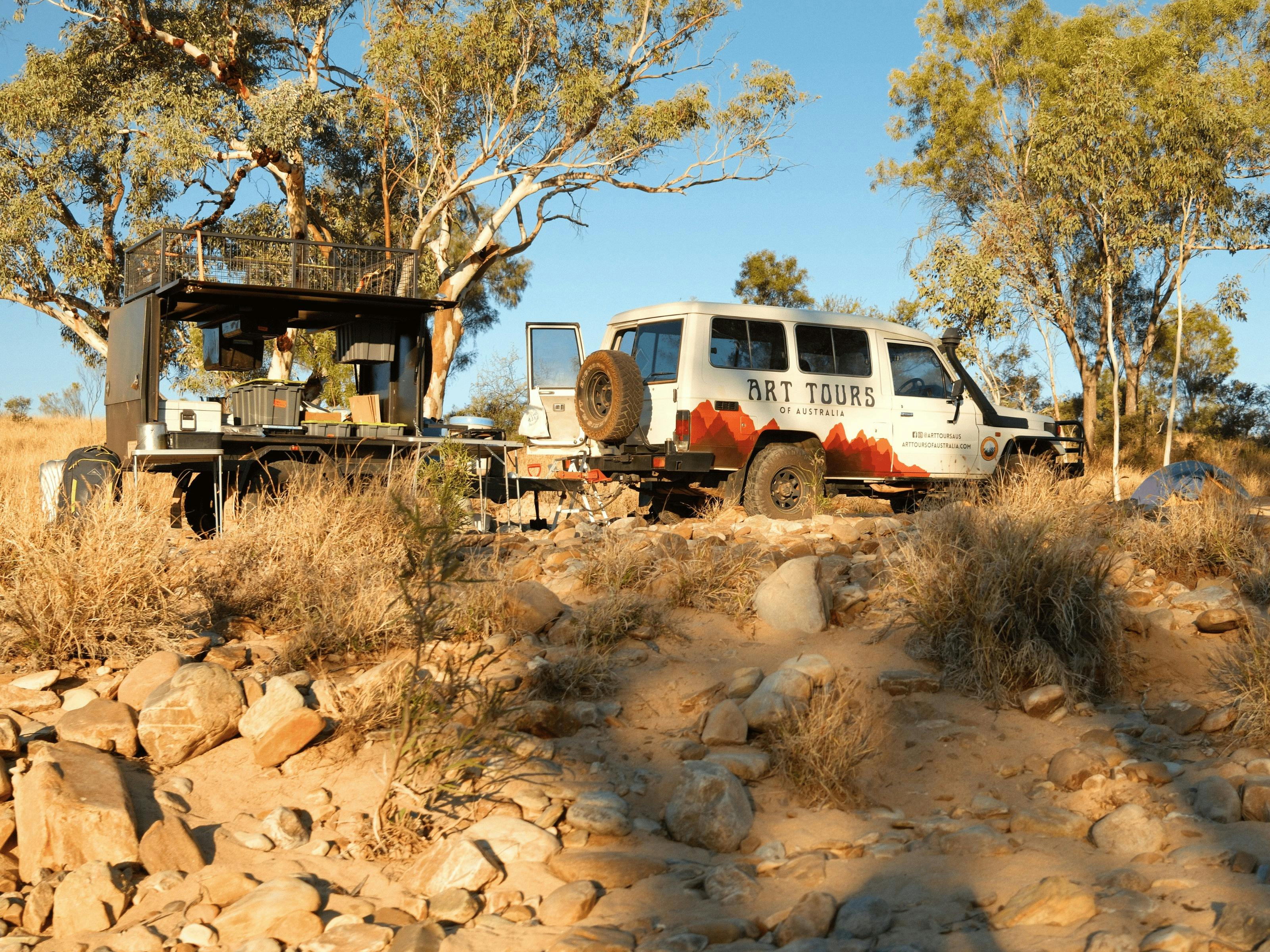 A branded 4WD with trailer parked in a rocky riverbed with white gum trees