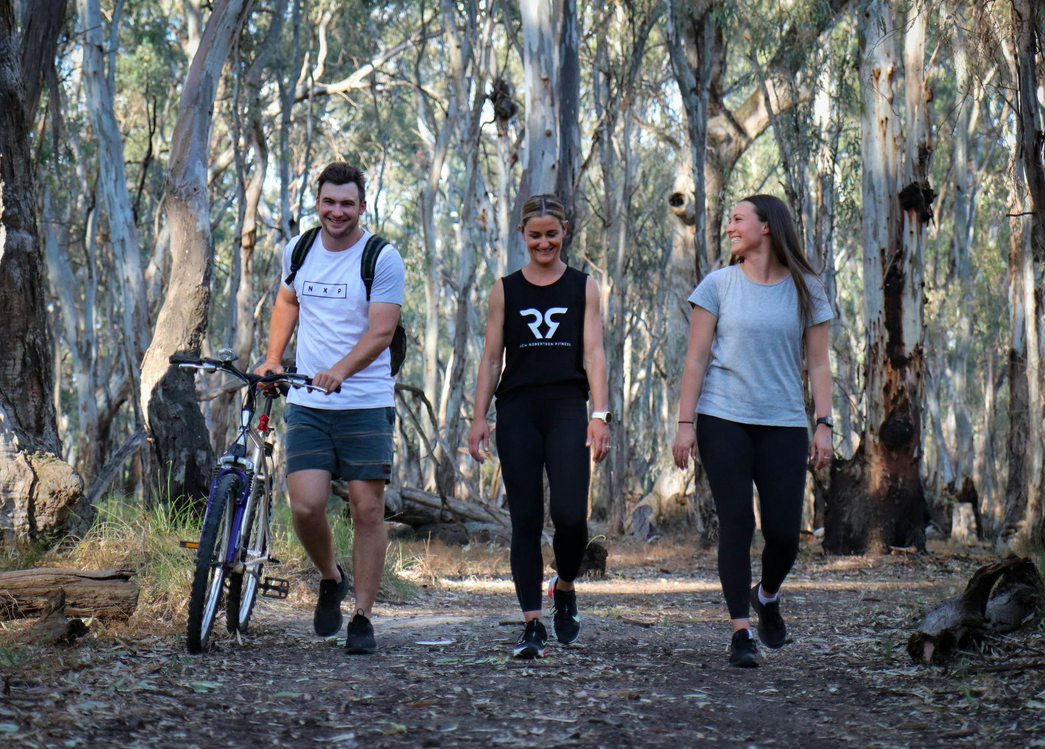 3 young adults hiking on a walking track in the Gunbower State Forest. One adult is pushing a bike