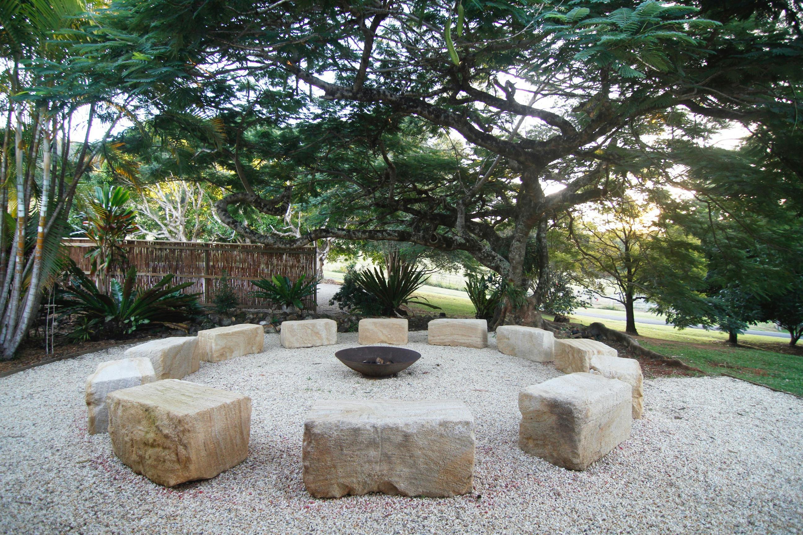A beautiful stone sitting circle with a fire pit in the middle and beautiful big tree