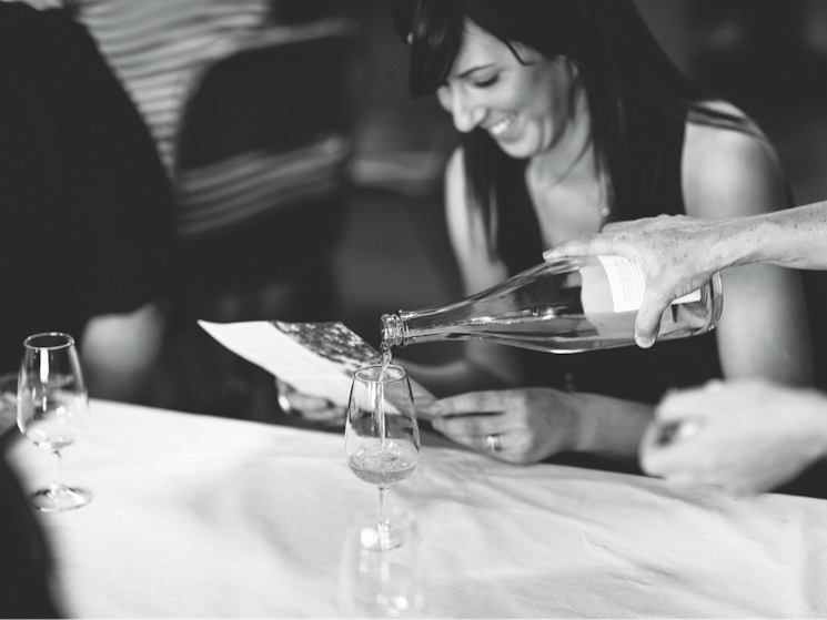 A young woman smiles broadly while reading a brochure and having cider poured for her in a cellar