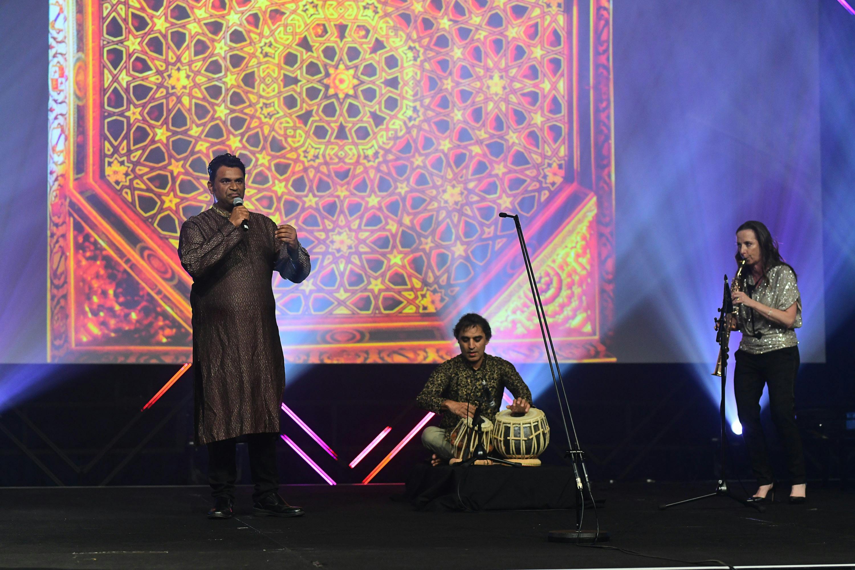 Three performers in front of a big screen