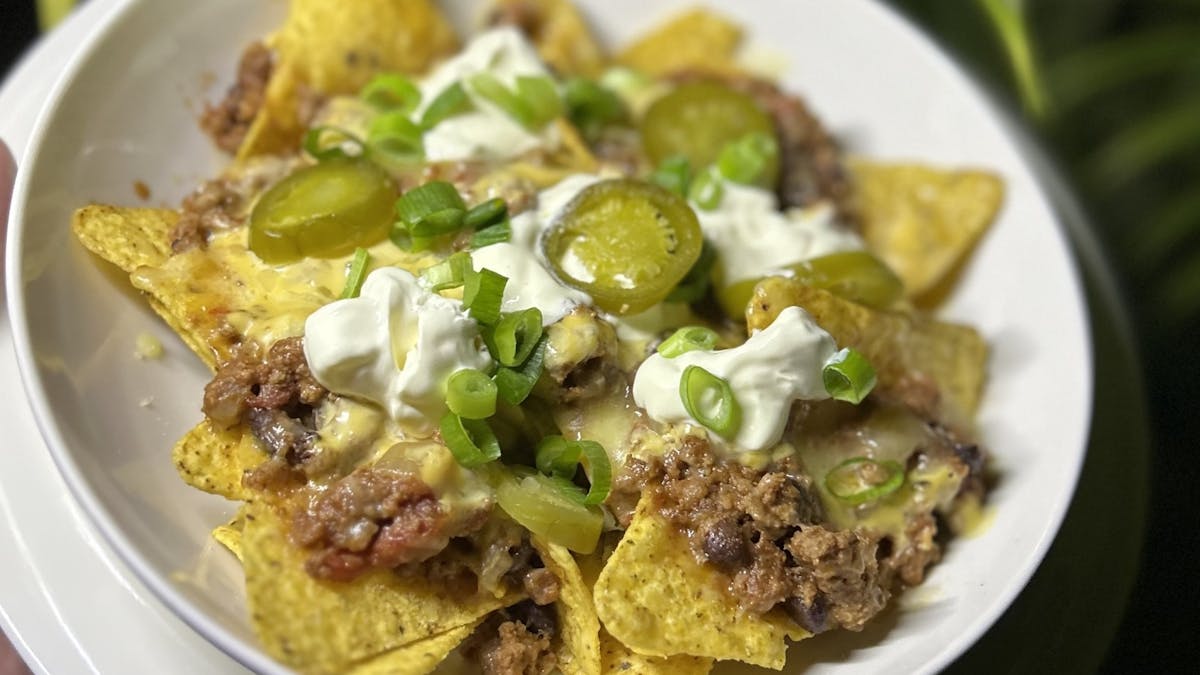 A white bowl filled with loaded beef nachos, topped with melted cheese, sour cream, sliced Jalapeno