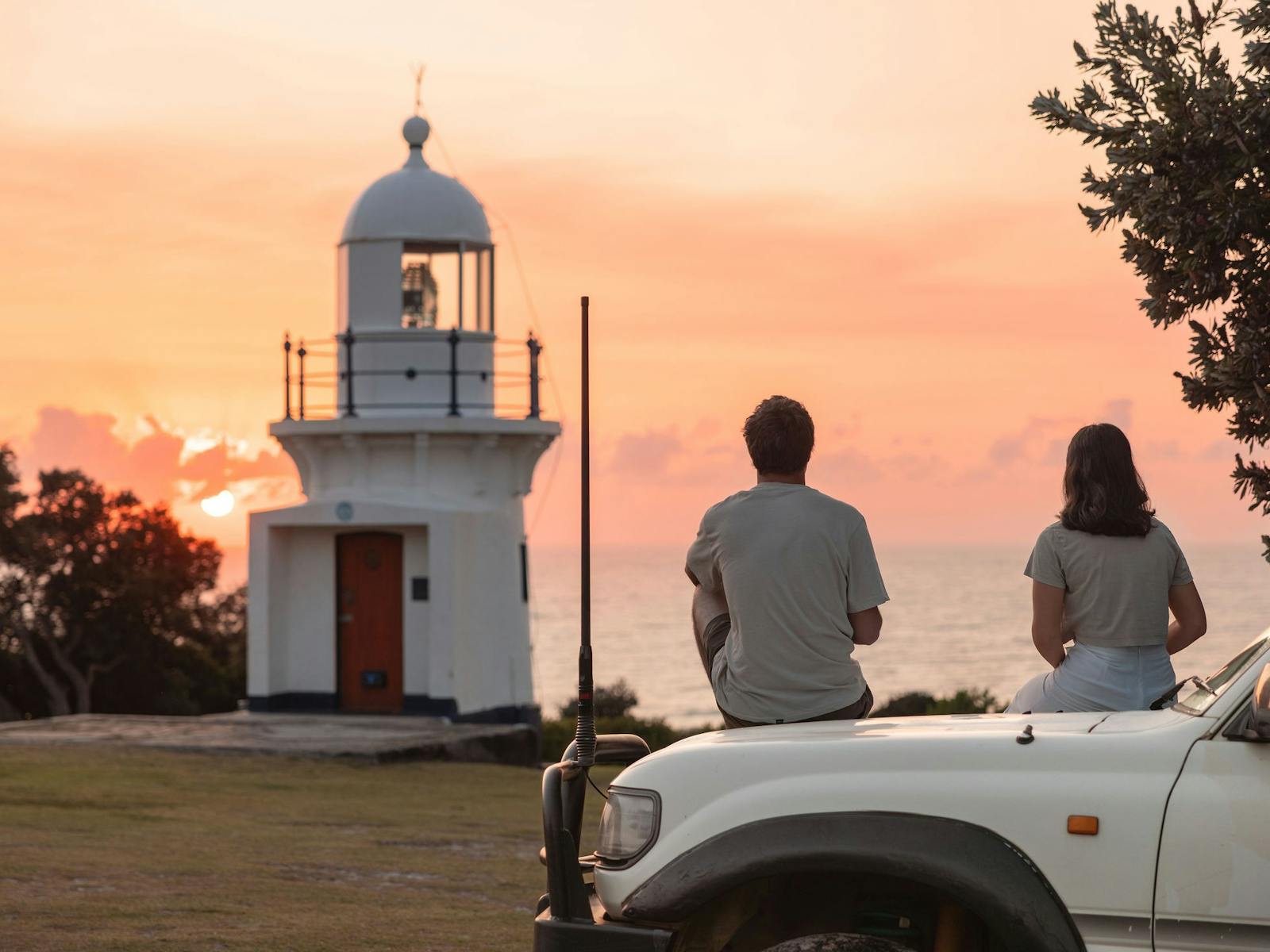 Couple sitting on bonnet of car looking at Lighthouse