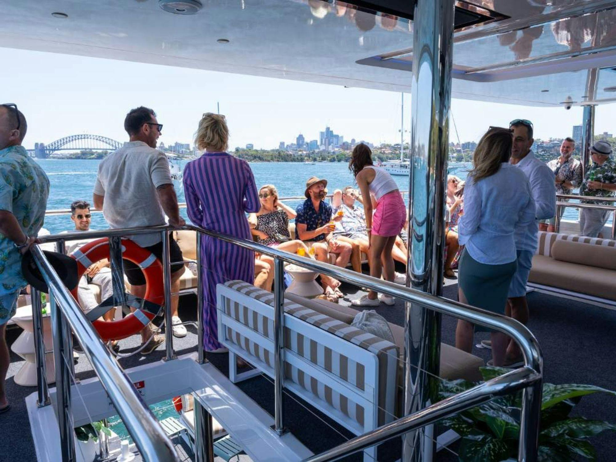 Guests socialising on the open deck of Karisma 2 with Sydney Harbour Bridge in the background