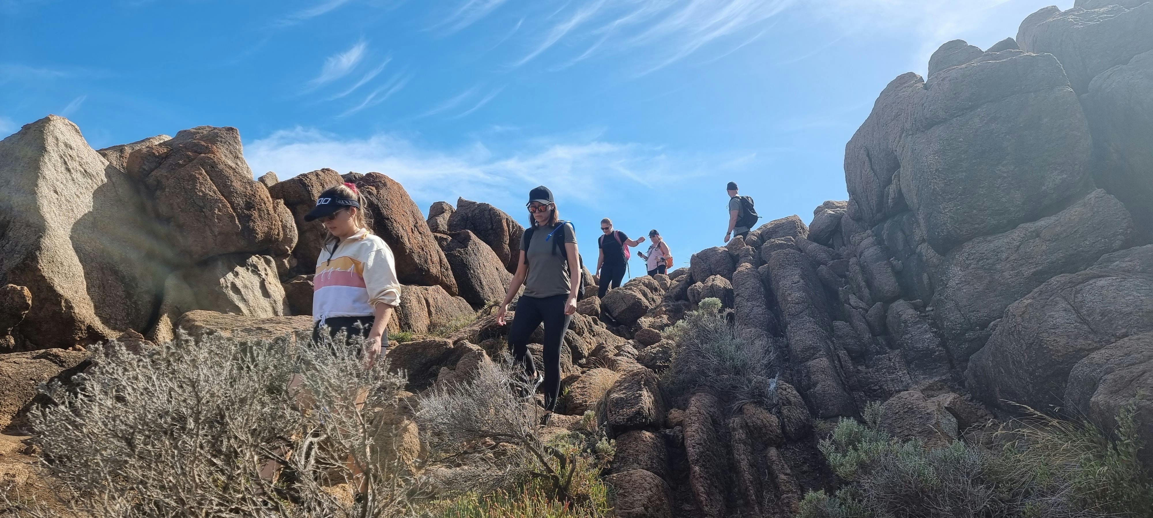 Hiking group walking through large rock formations on sunny day with clear sky