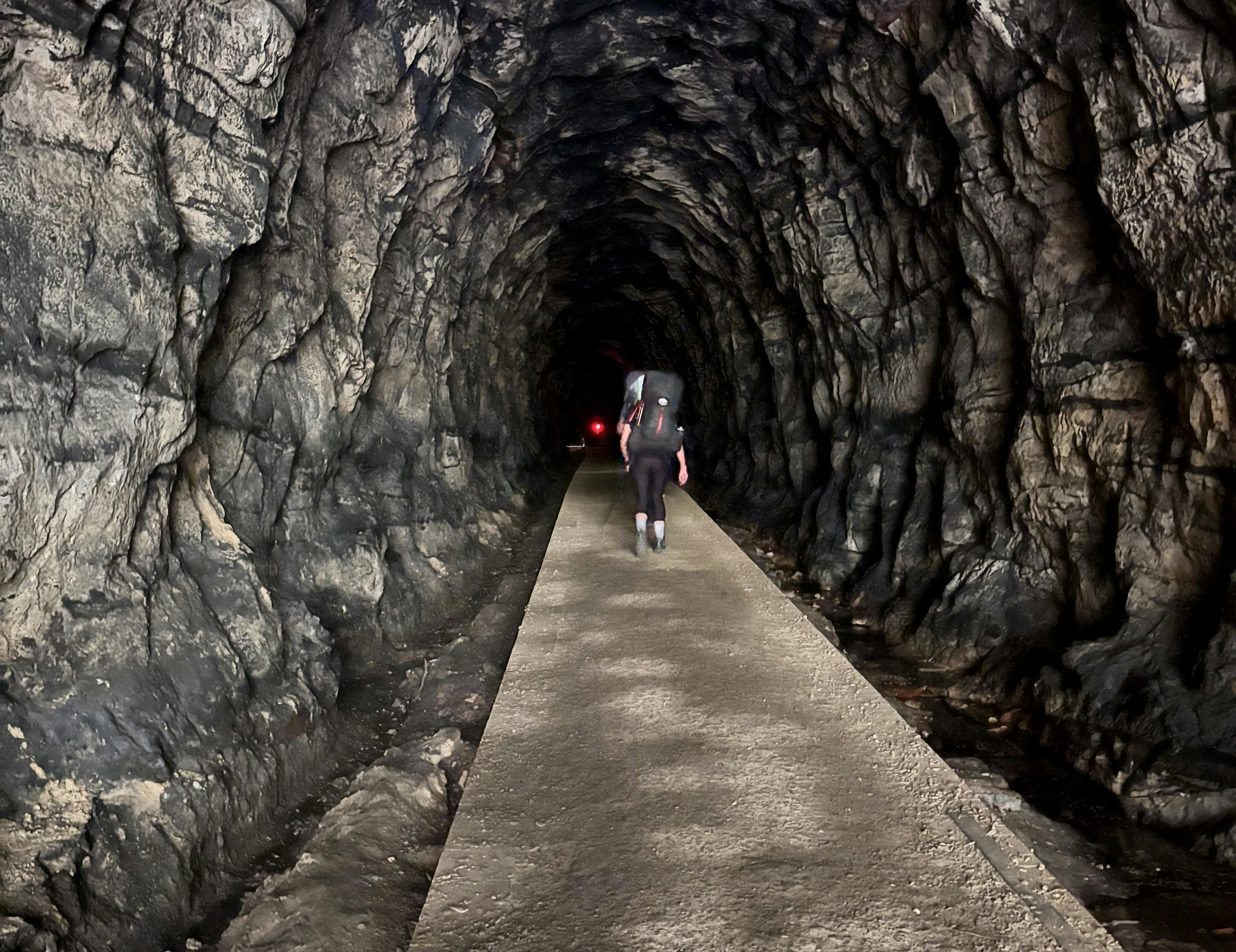 A woman with backpack walking along a path in a dark railway tunnel. now home to 1000s of glow worms