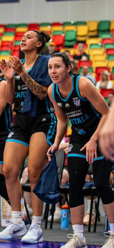 Four basketball players cheer while sitting on the side of the court.