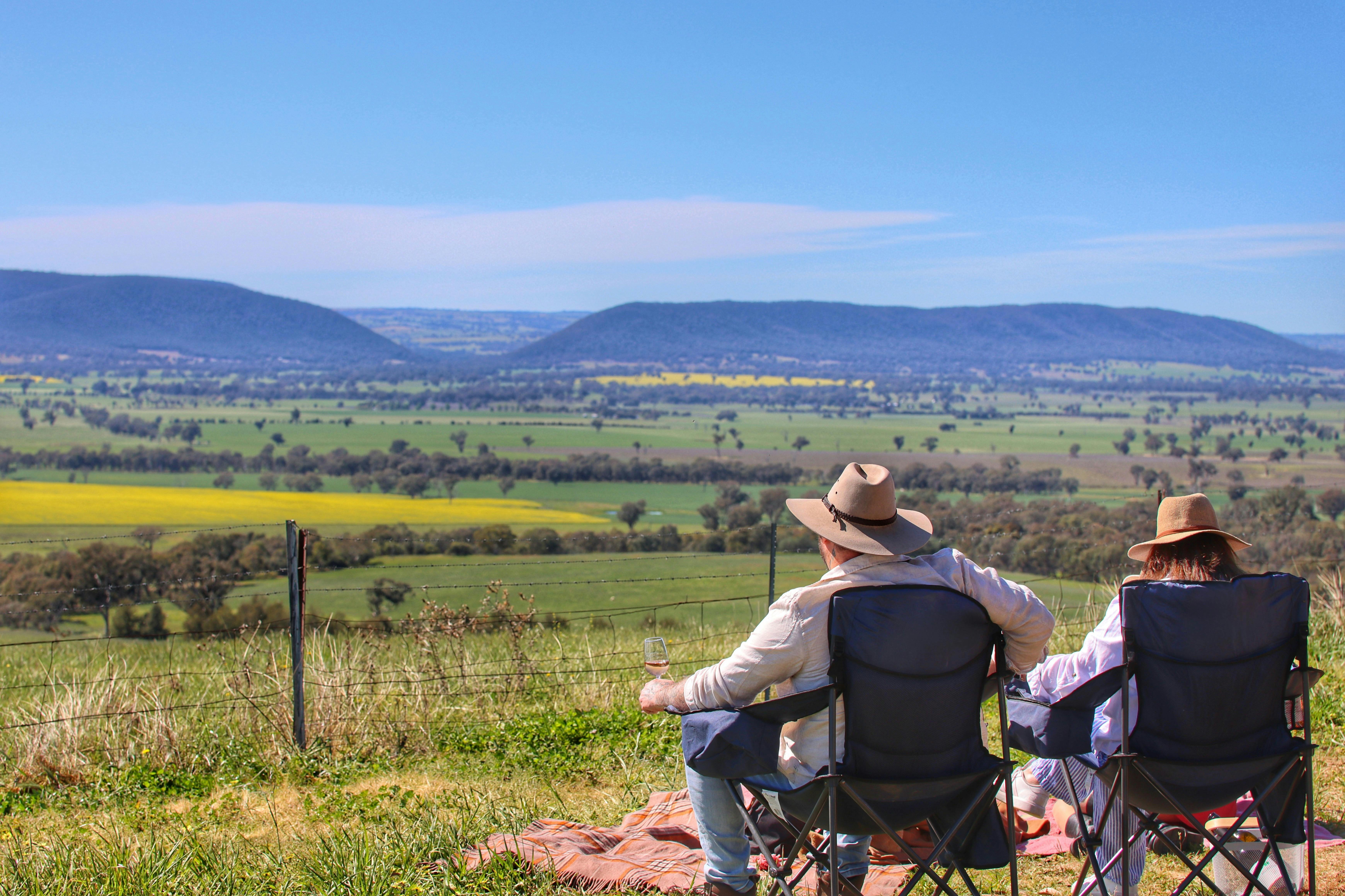 Ein Mann und eine Frau sitzen in Picknickstühlen und blicken während der Rapssaison auf die Landschaft.
