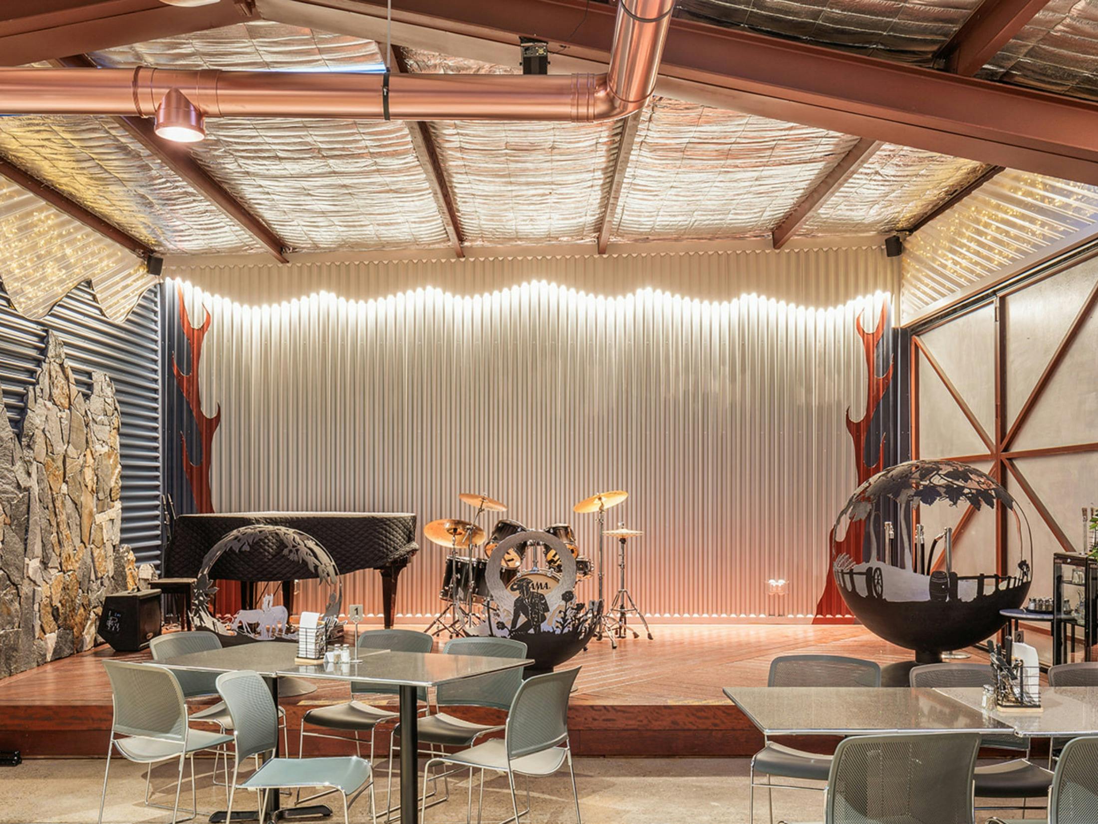 Stage with drum kit, piano and rustic hand-made fire pit display. Live music Friday & Saturday night