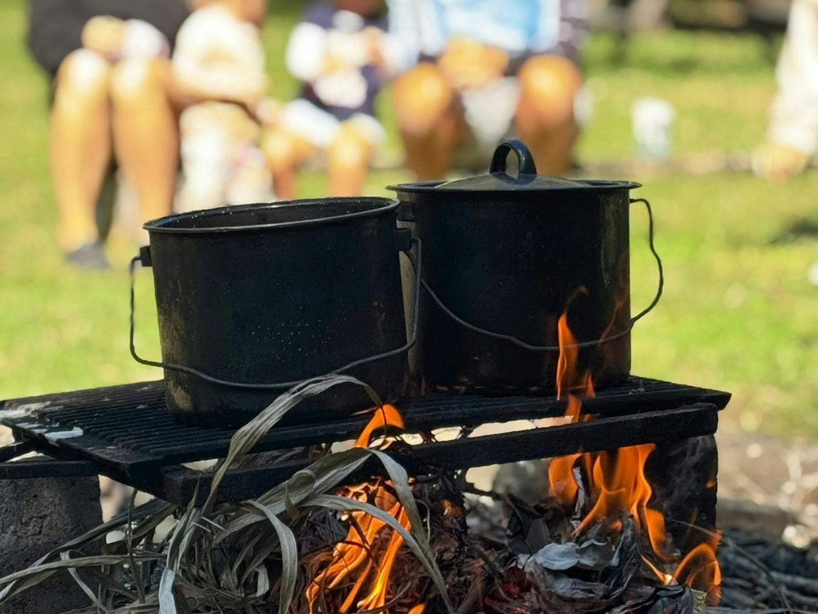Families sitting near a cooking pot on a campfire at Birdwings Forest School