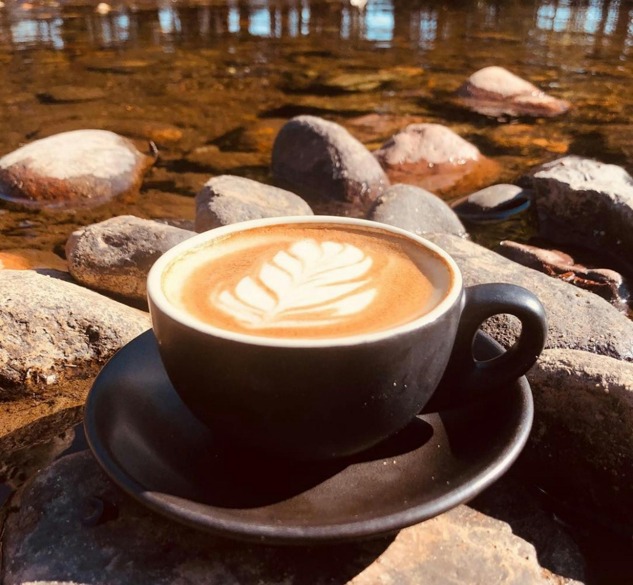 A coffee cup, with milk foam design, sitting on the bank of the Tumut River
