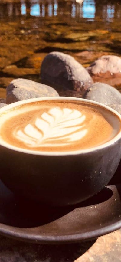A coffee cup, with milk foam design, sitting on the bank of the Tumut River