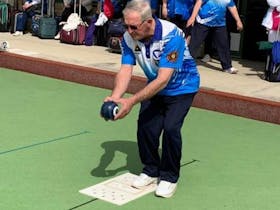 A man lining up with his bowling ball in his hand concentrating on sending his bowl down the lawn.