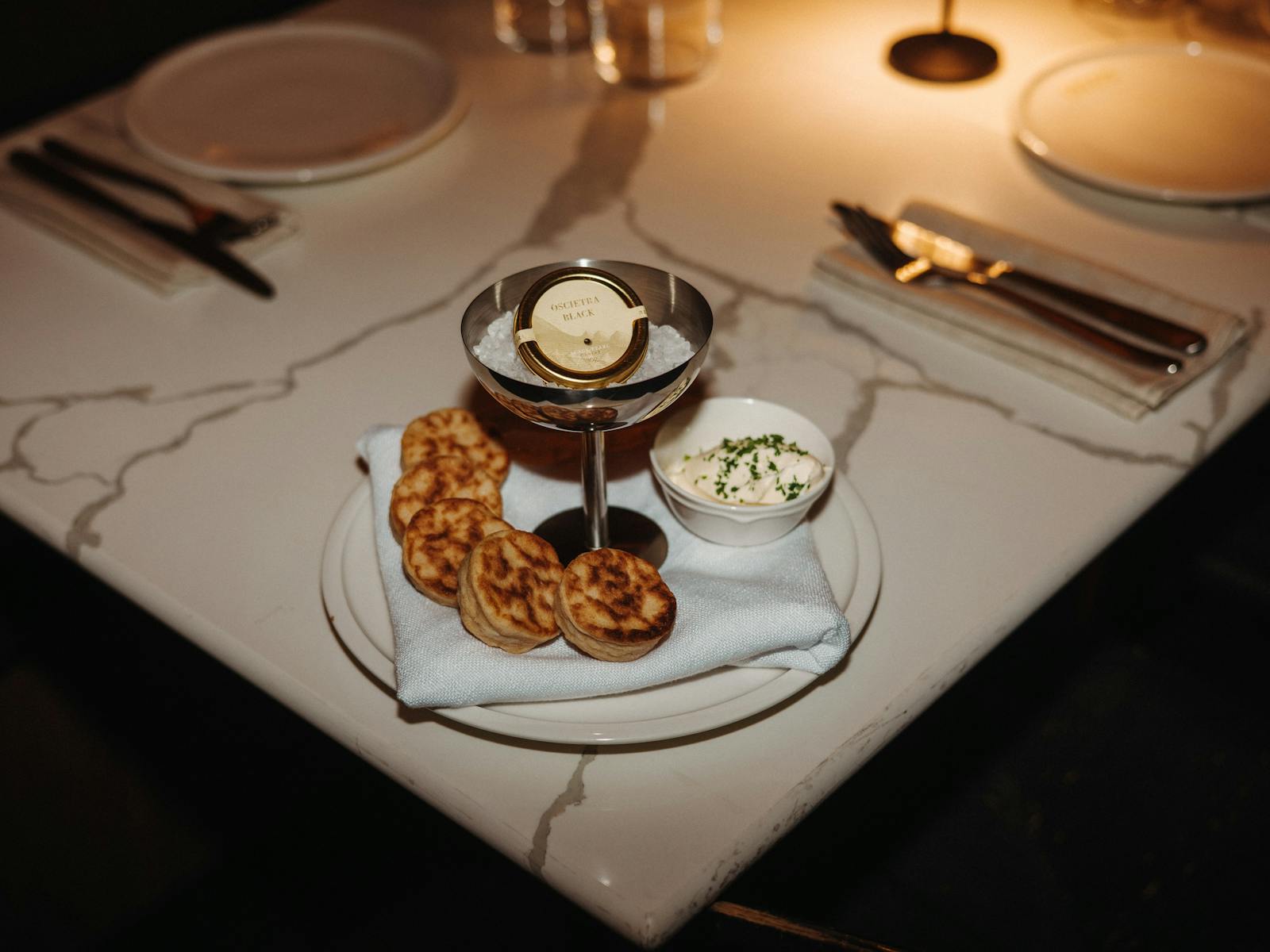Caviar in a silver cup on a plate with small crumpets on it