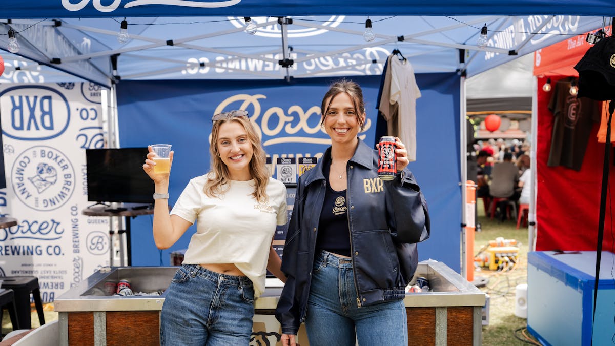 Two girls holding beers smiling at the camera