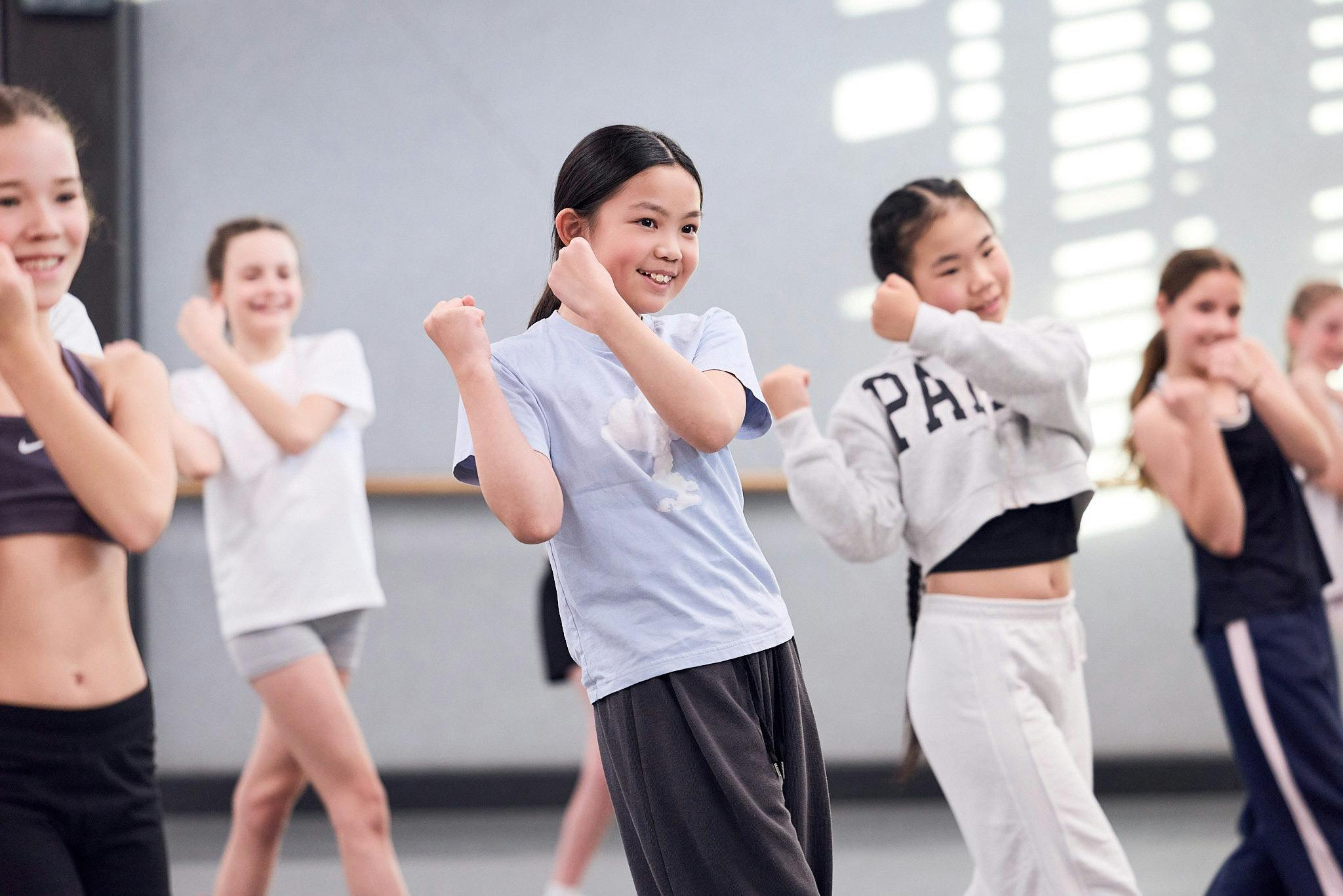 Young female is dancing in a class. There are other dancers around her