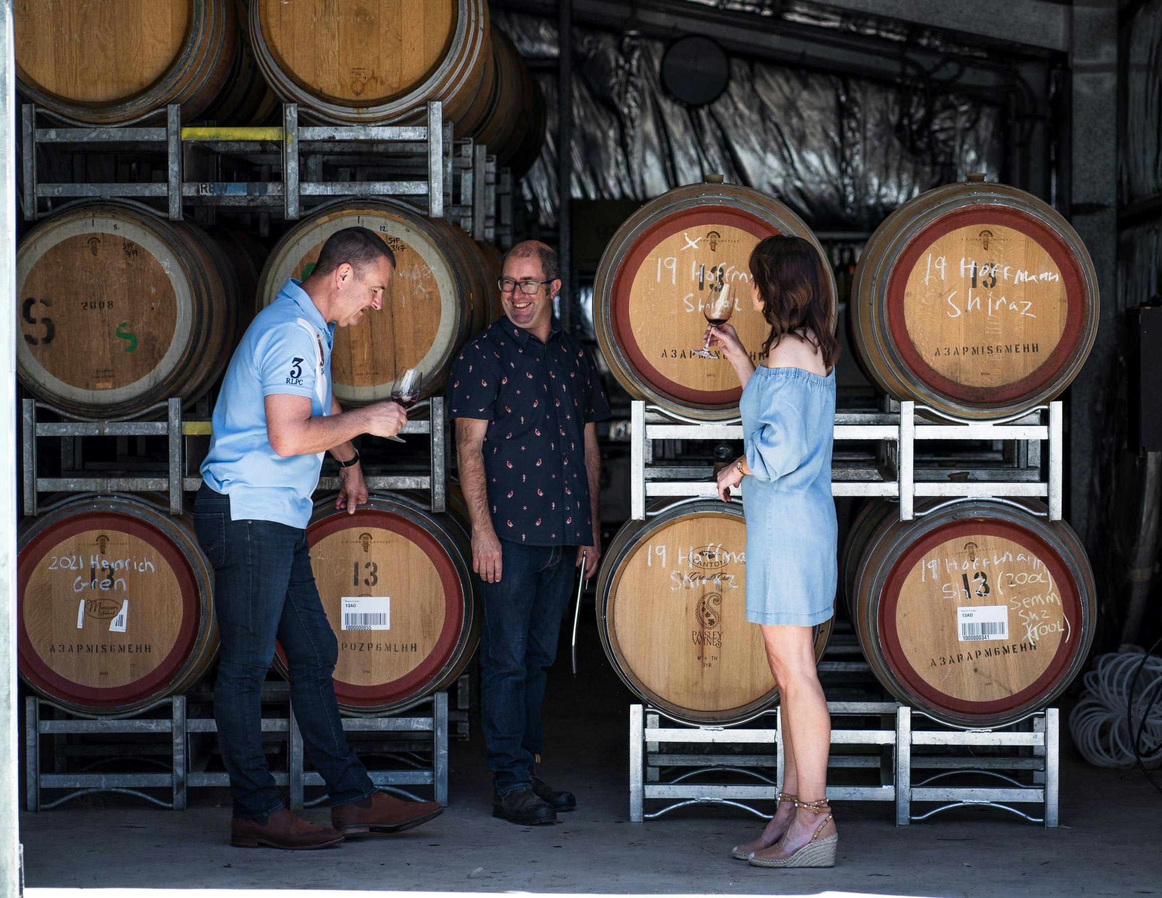Derek with guests standing with wine barrels, tasting wine