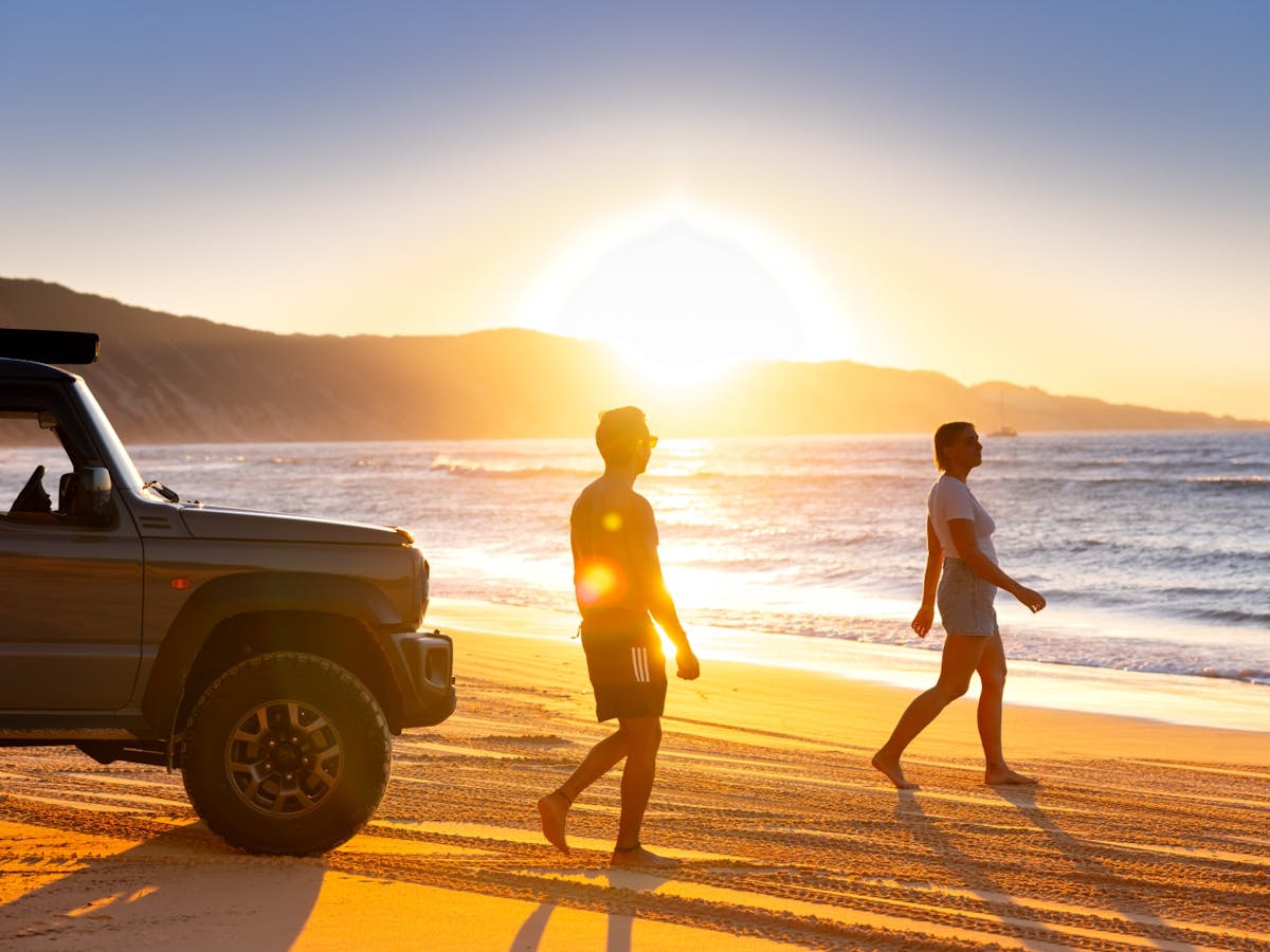 A couple with their car on the beach as the sun sets
