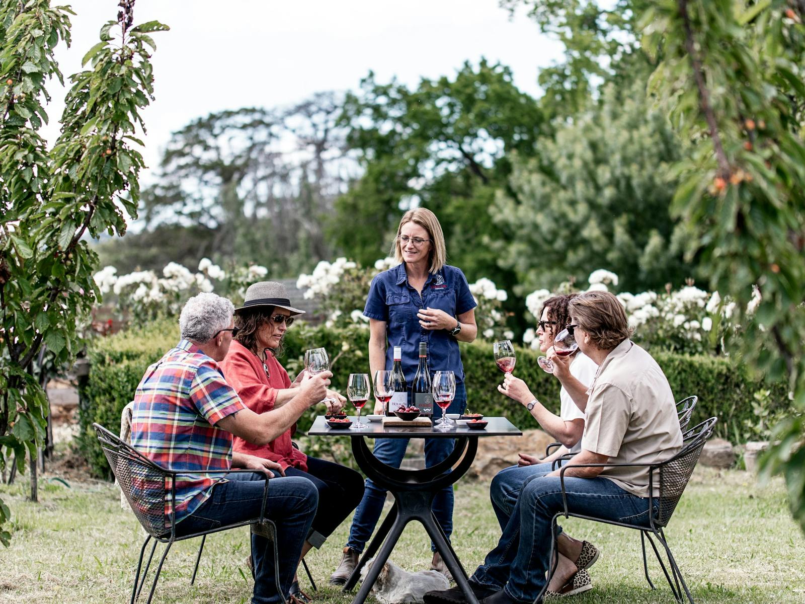 Winemaker, Bec Duffy with four guests at outside table in the Holm Oak Garden doing wine tasting