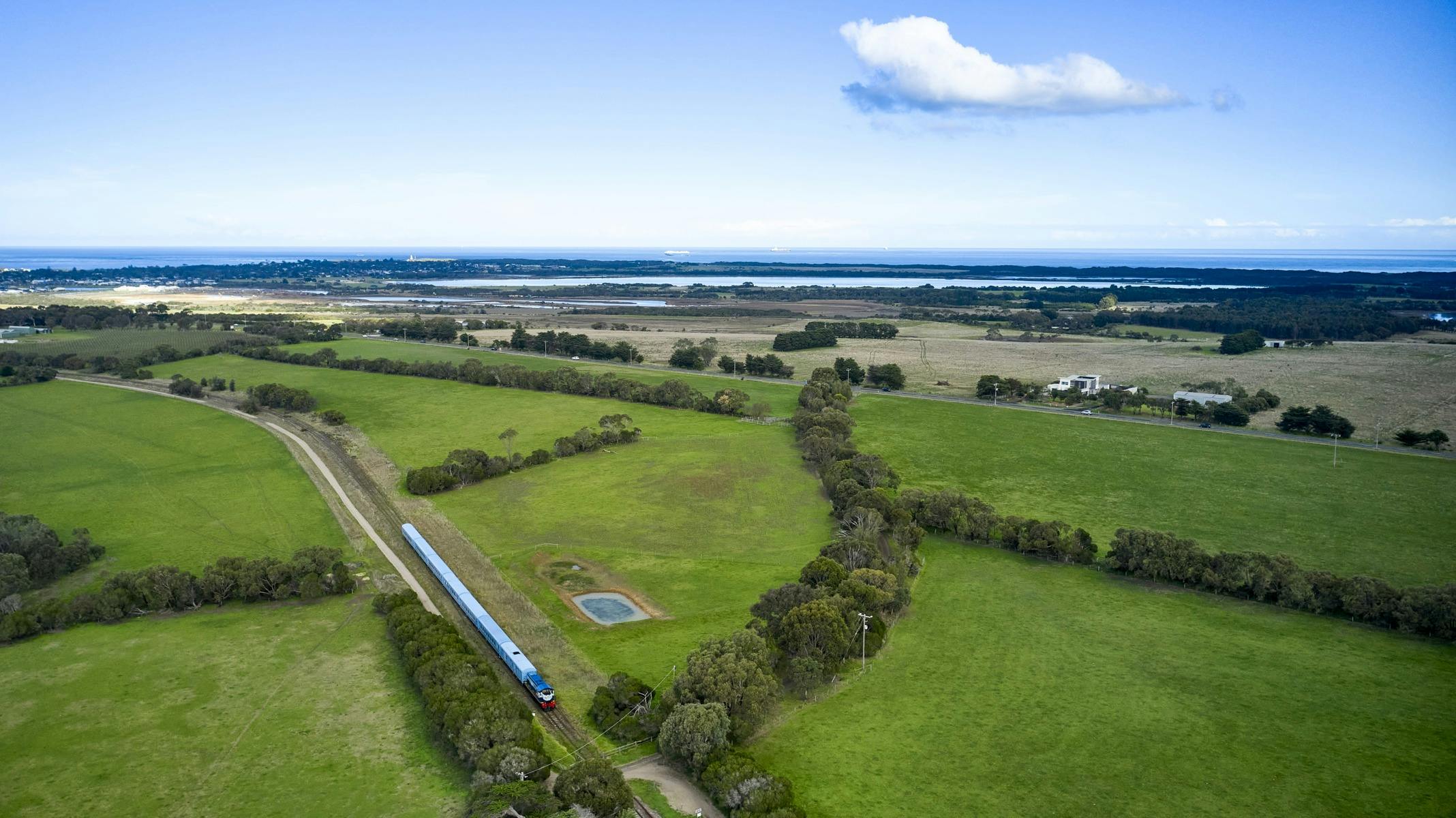 Blue train with 8 carriages and diesel locomotive passes through farmland