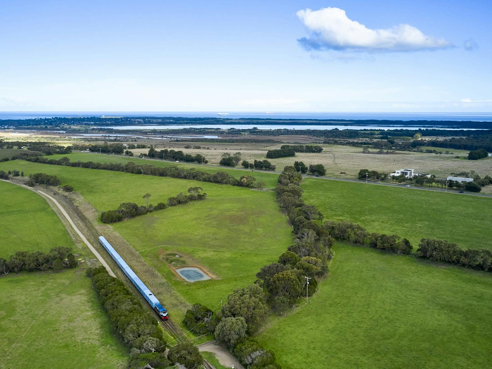 Blue train with 8 carriages and diesel locomotive passes through farmland