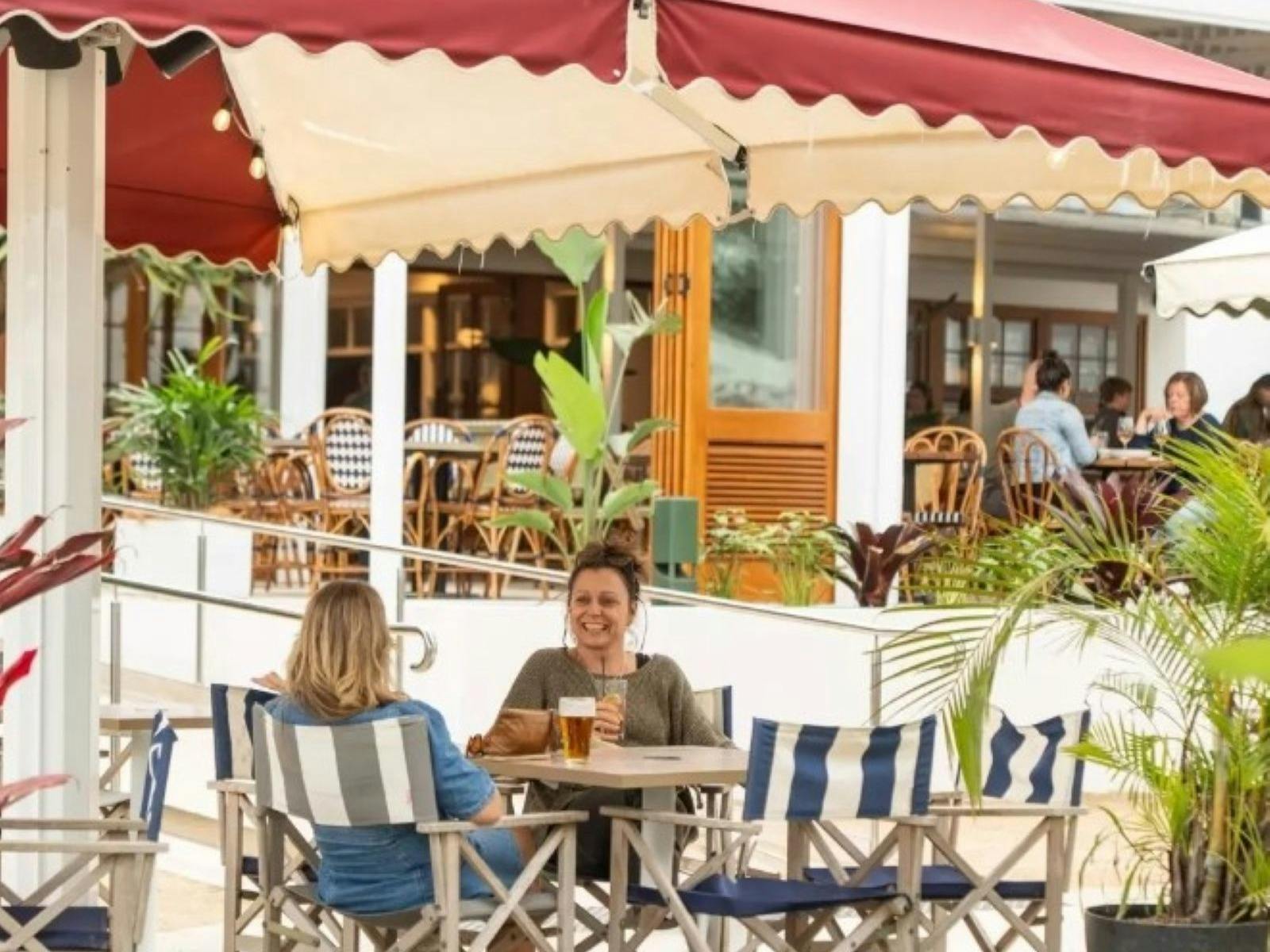 two women at under umbrella outside seating chatting