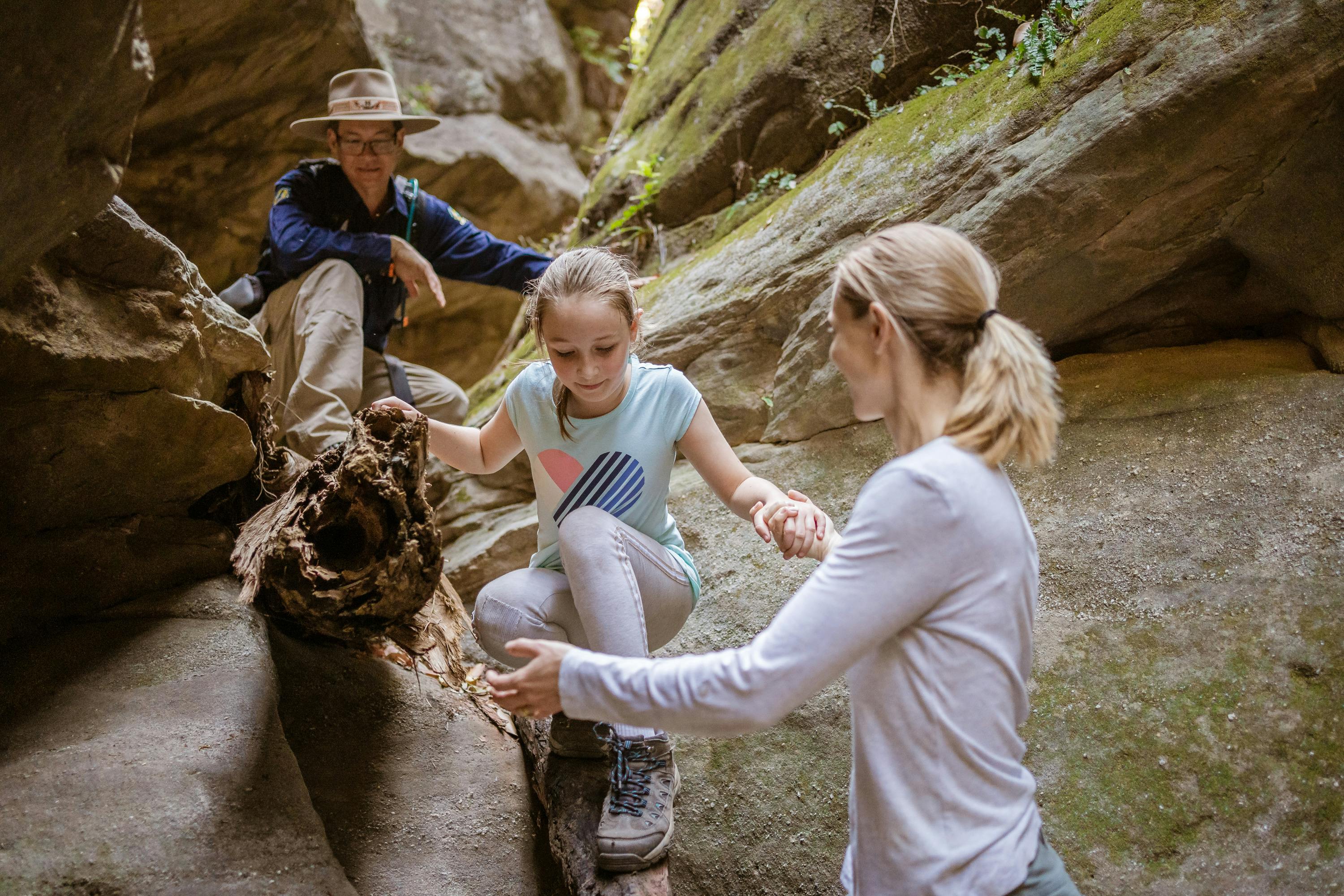 A mother assists her daughter as she navigates an obstacle in a slot canyon at Carnarvon Gorge.