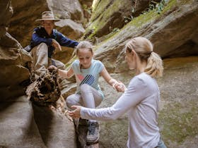 A mother assists her daughter as she navigates an obstacle in a slot canyon at Carnarvon Gorge.