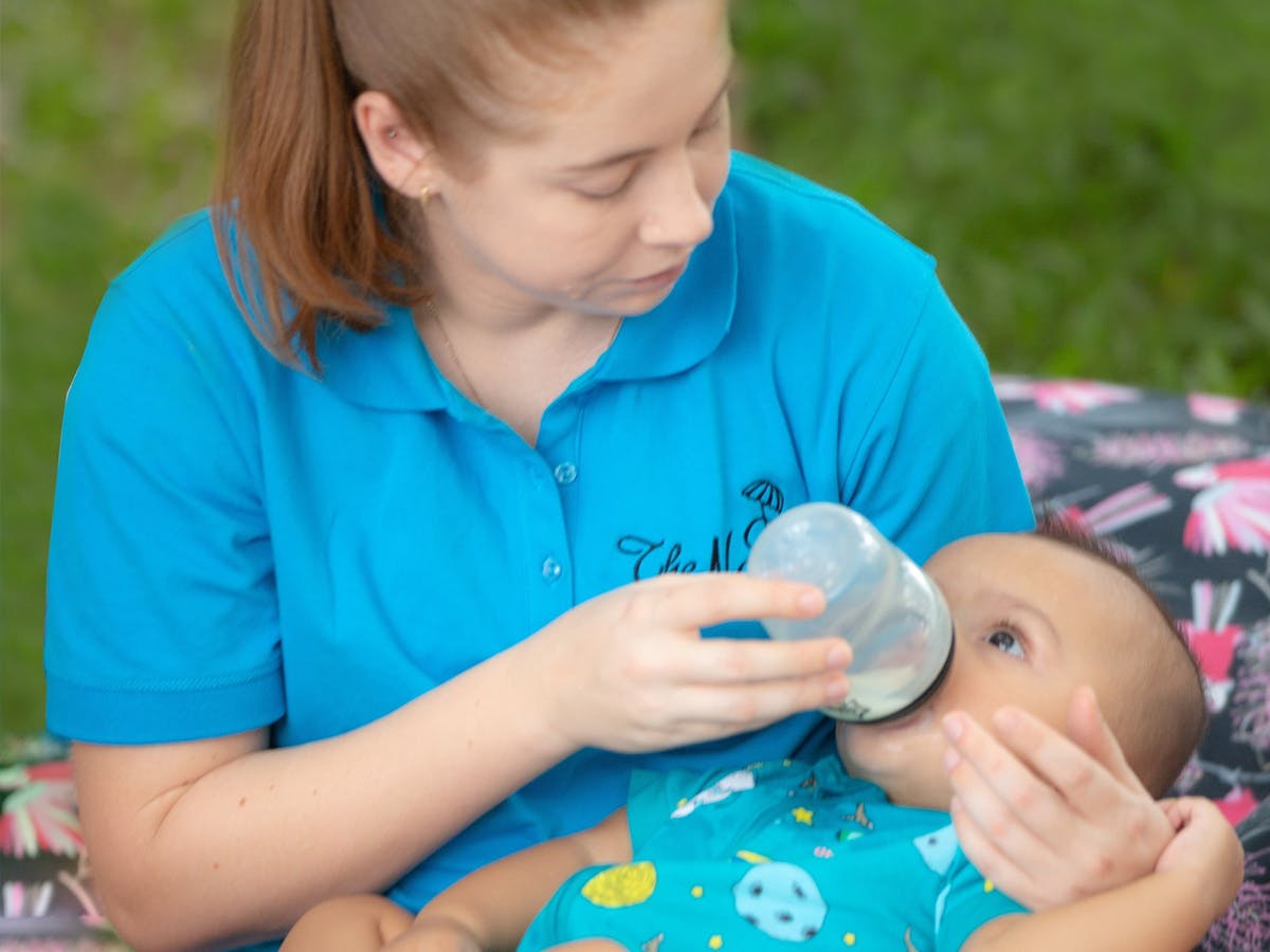 Nannies On A Mission feeding a young baby at a picnic