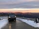 Double Black Alpine Mercedes drives up a snowy road on Mount Buller. Alpine peaks in the distance.