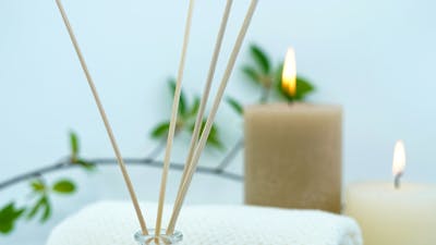 Reed diffuser, towel and lit candles against a white backdrop.