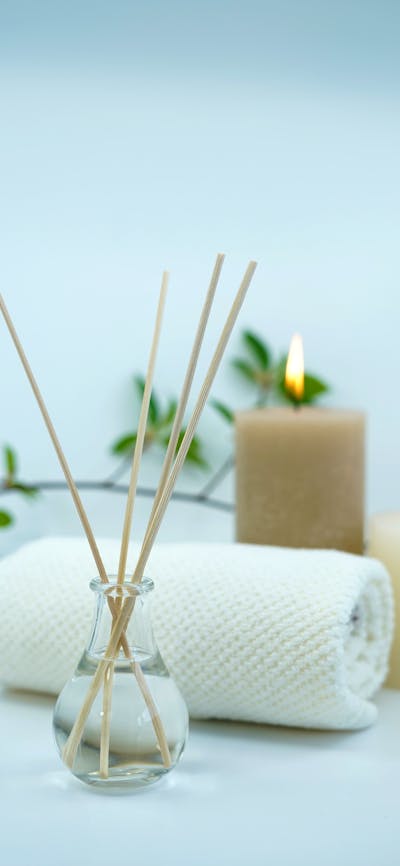 Reed diffuser, towel and lit candles against a white backdrop.