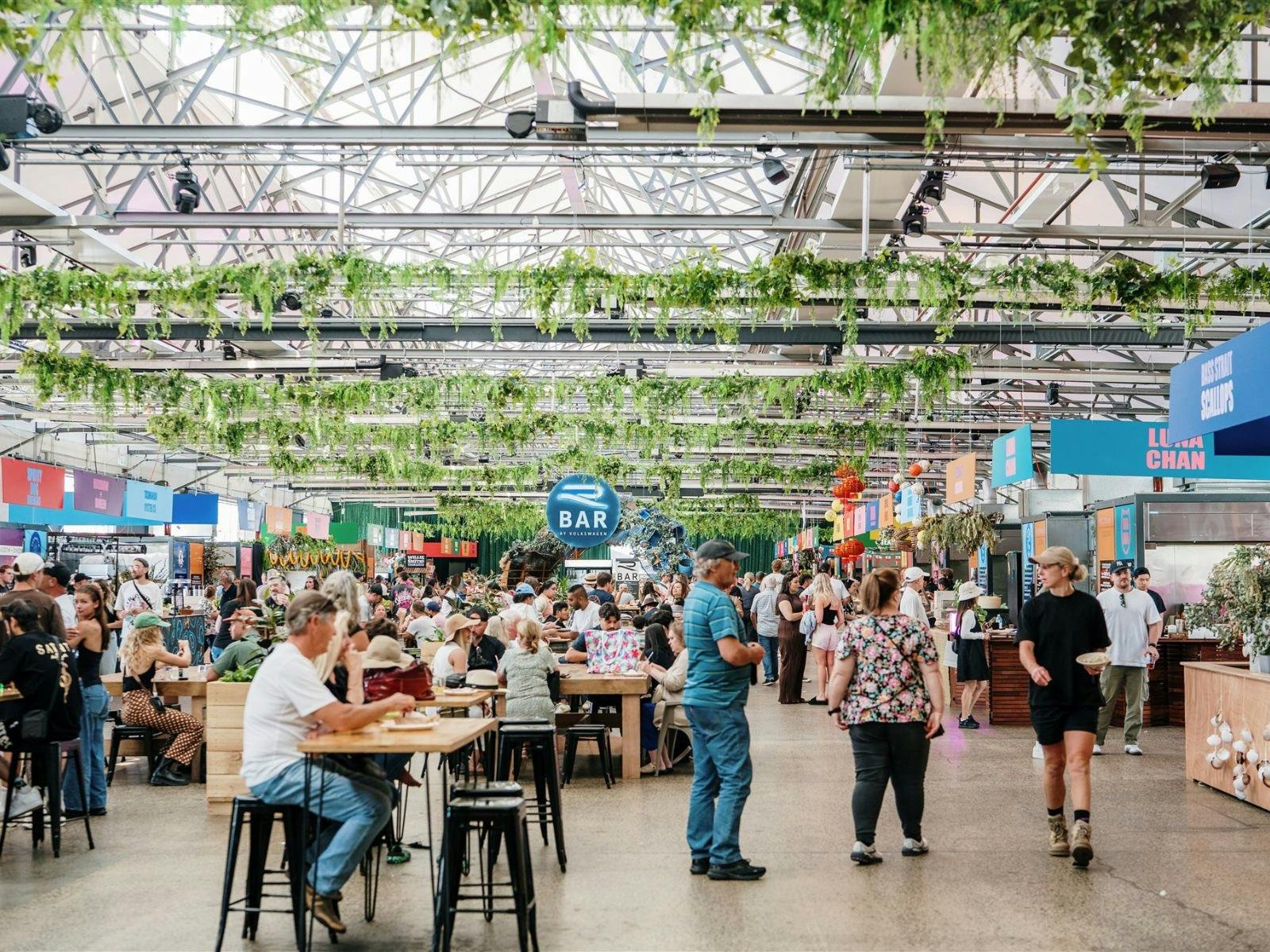 Visitors browse food stalls inside a large shed decorated with greenery.