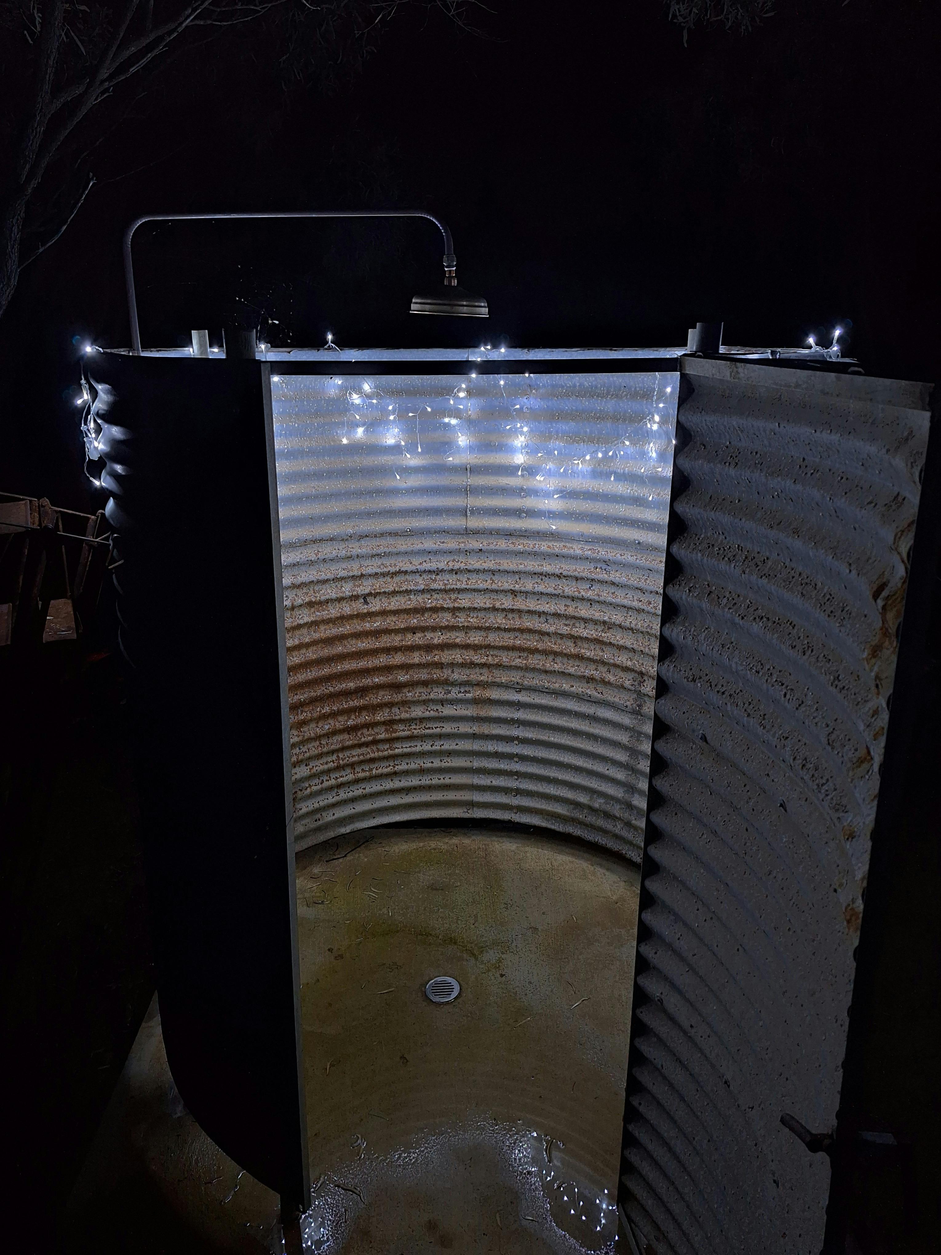 A corrugated iron tank made into an outdoor shower at night, lit with fairy lights