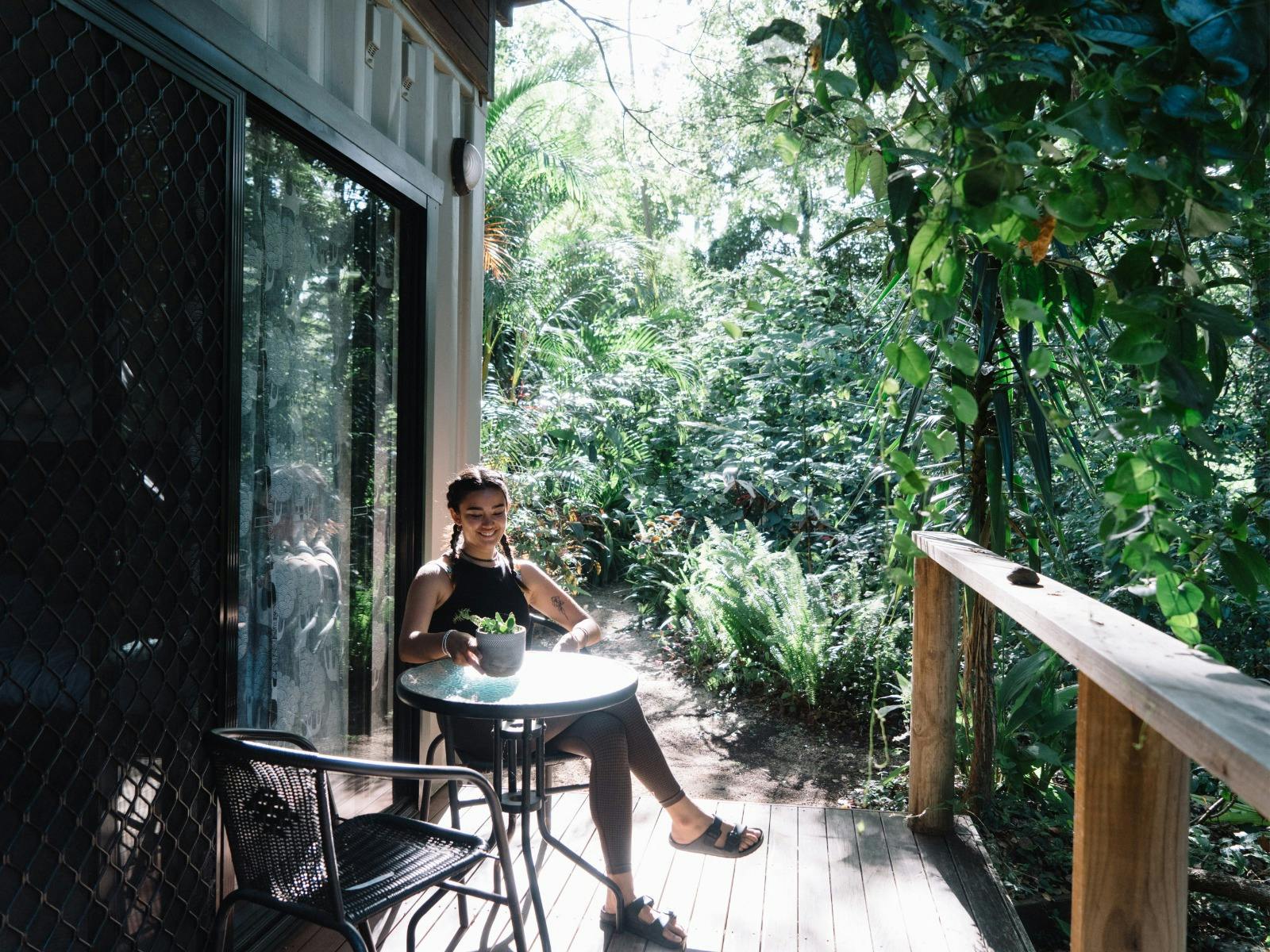 A woman is sitting in front of her room, overlooking nature and reading a book