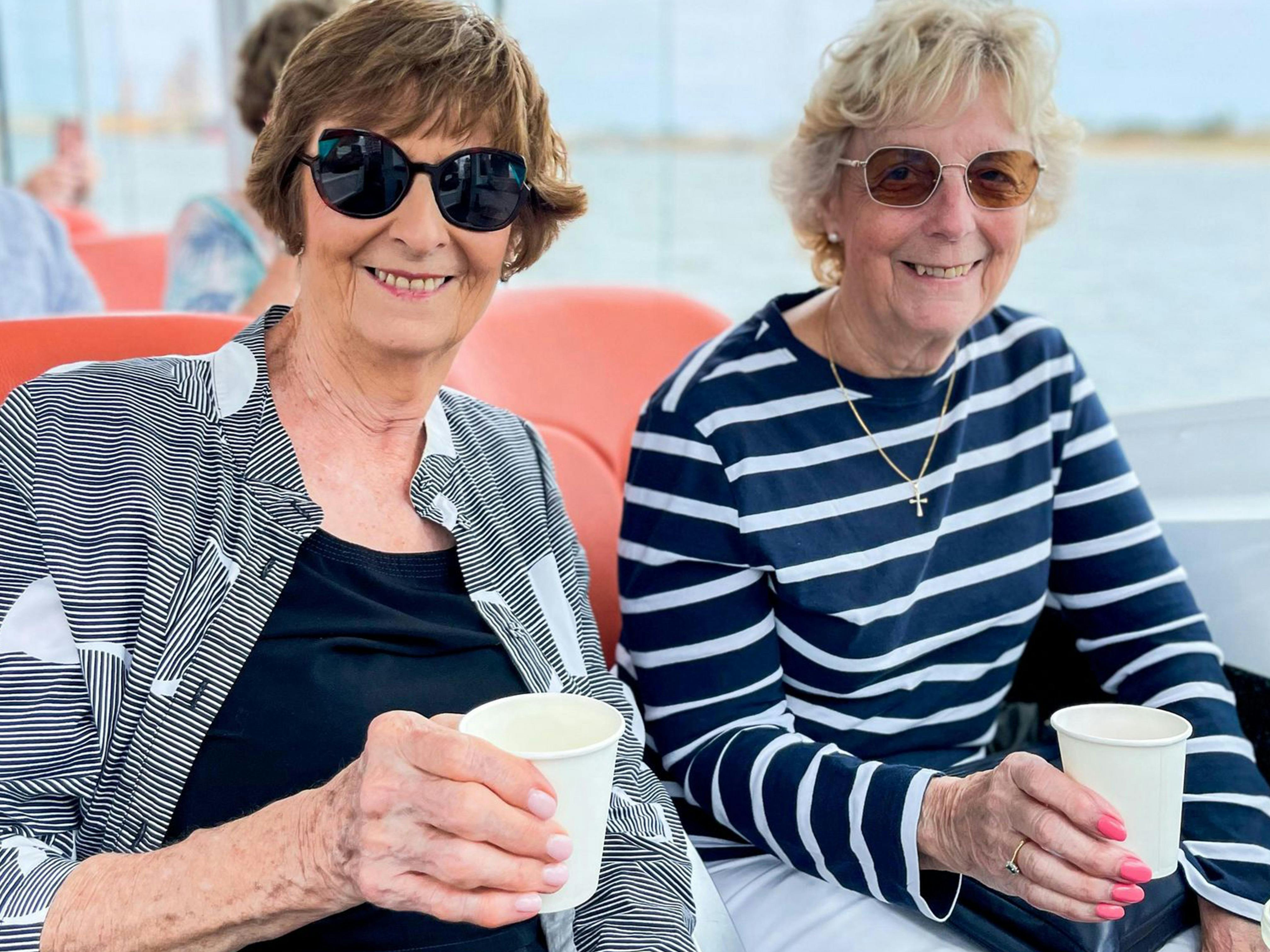 Two ladies smile at the camera, complimentary drinks in hand