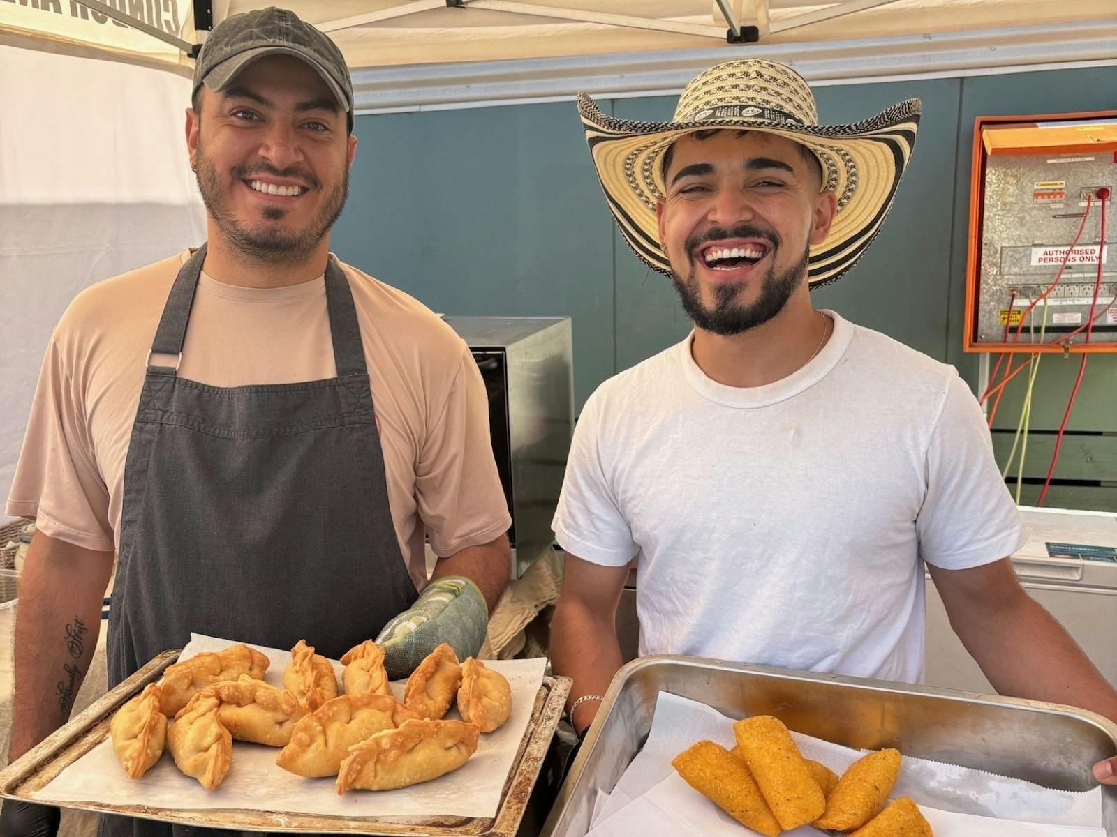 Two men holding freshly cooked food at a stall