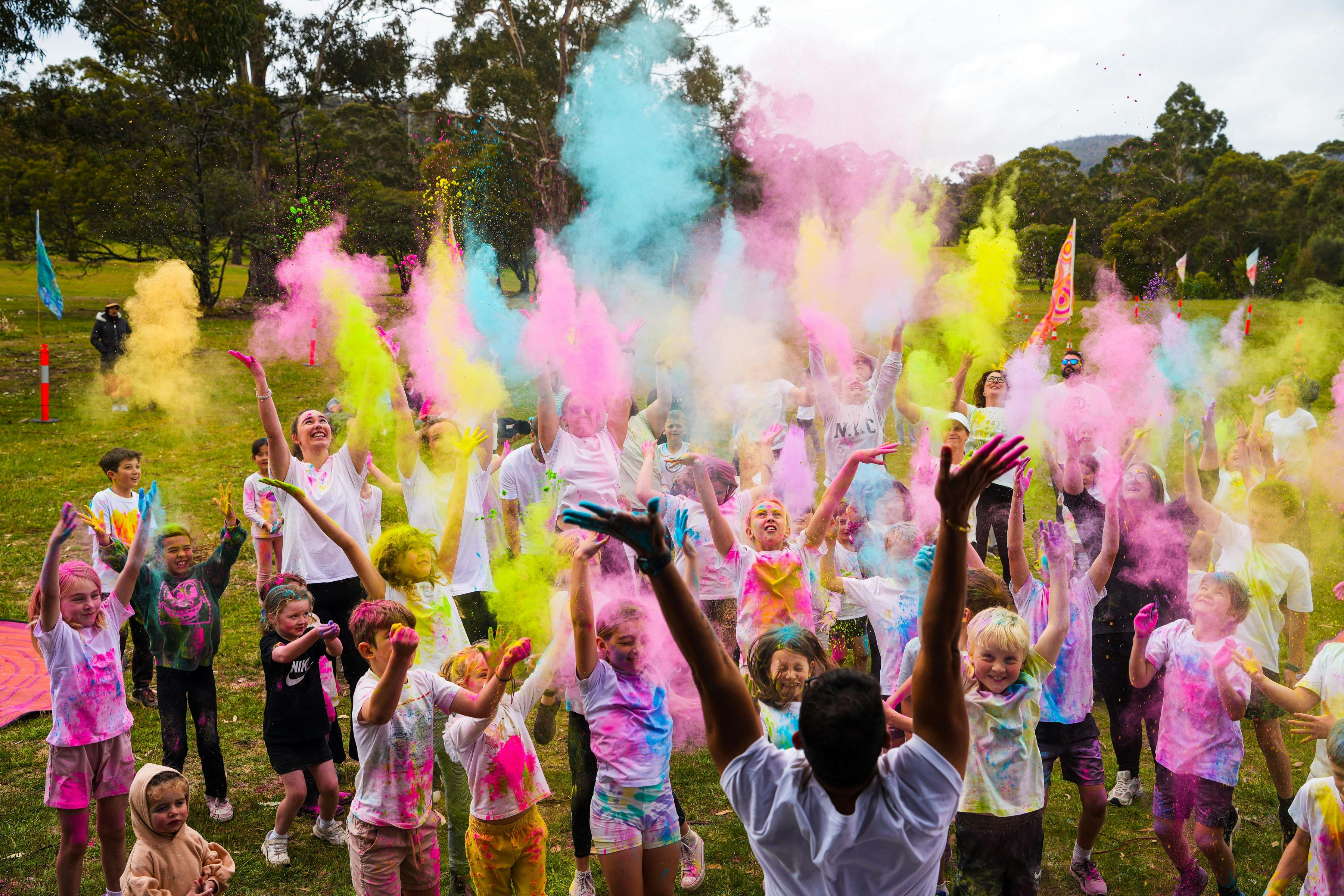A group of children and adults throwing coloured chalk dust in the air simultaneously while smiling.