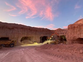 Open-cut opal mine with machinery under a pink sunset sky