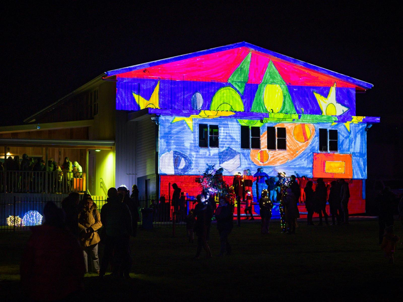 A colourful children's artwork is projected on the outside of a building.