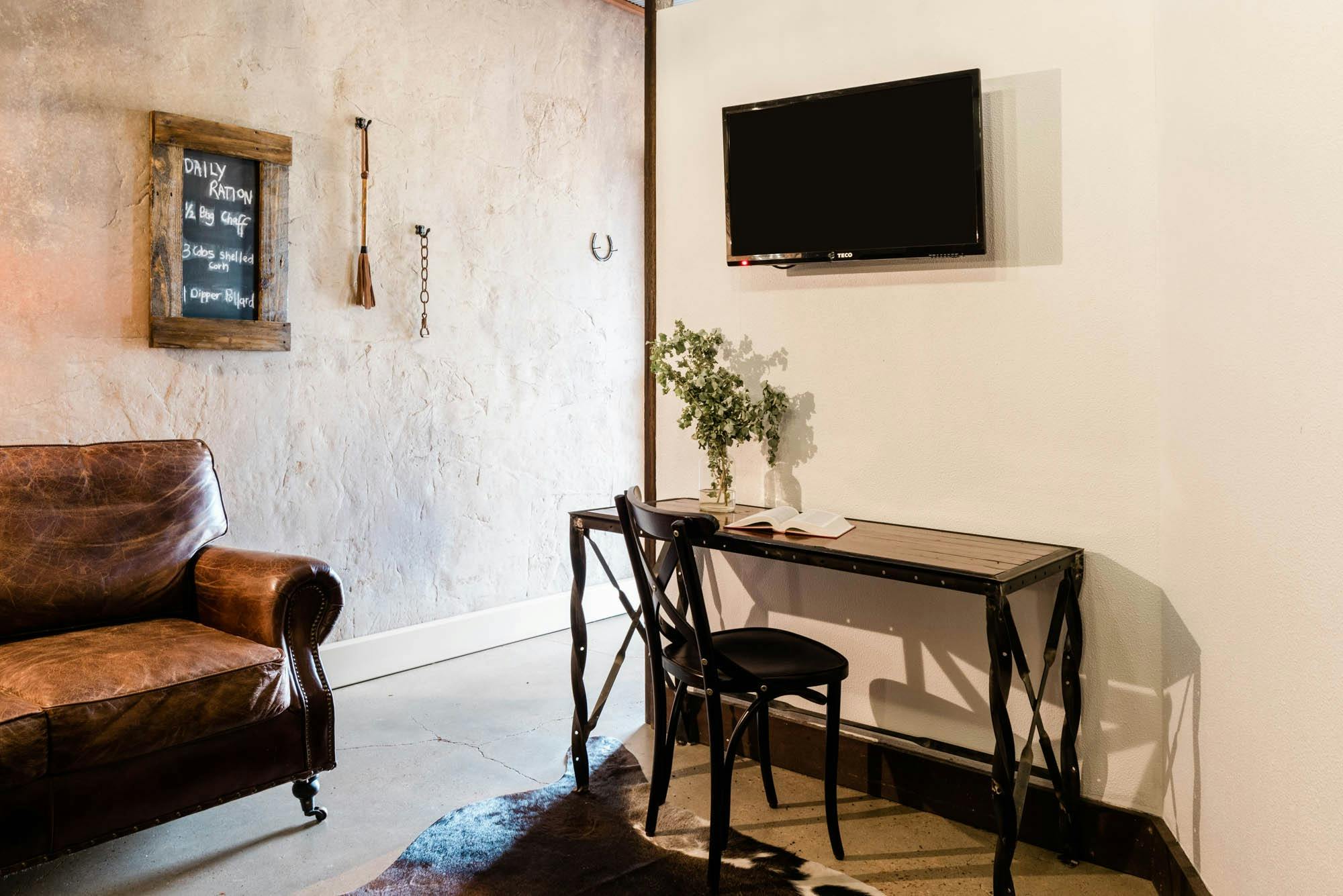 Small desk and chair in rustic room with cement walls and cow hide floor mat