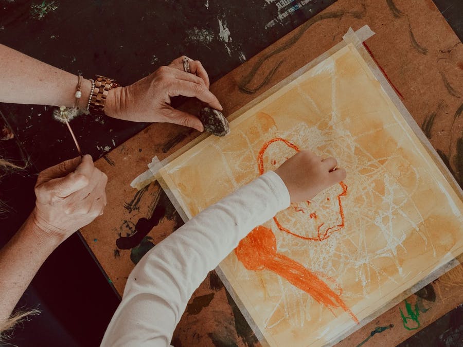 Carer and child collaborating on an orange crayon drawing